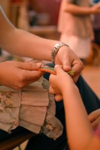 Detalle de las manos de una maestra waldorf y una niña haciendo trenzas con lana de colores