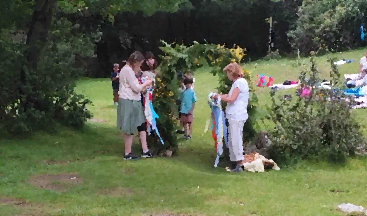 Alumnos waldorf de la escuela infantil grimm en la fiesta de san juan de final de curso pasando por un arco hecho de flores y helechos